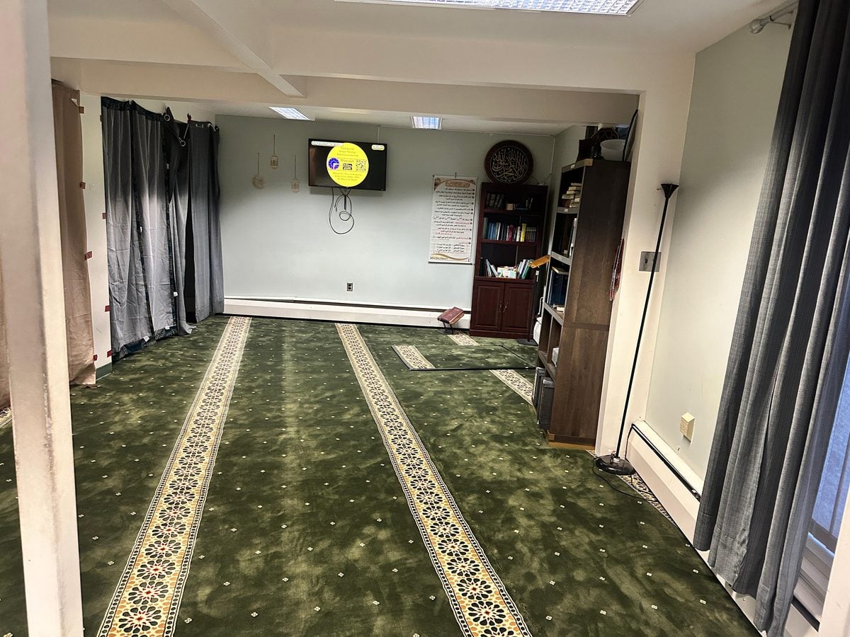 The prayer room at the MSA Community Center, with new green carpet and prayer rows, a TV on the far wall and bookshelves