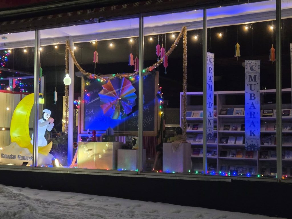 The Storytelling Center's front windows at night, decorated with paper lanterns, Ramadan Mubarak banners and a glowing crescent moon.