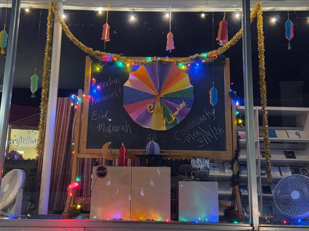 A chalkboard in the window reads Ramadan Kareem, Eid Mubarak and Community Meal 3/19/26 under colorful paper decorations.
