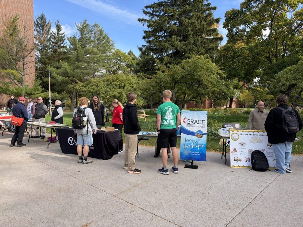 Visitors stop at faith group tables along the Commons on a sunny fall day, with the MSA display board at right.