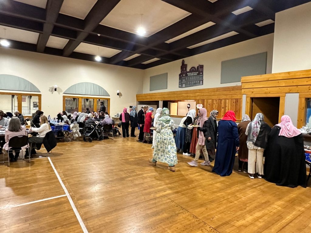 Women in colorful headscarves line up at the buffet as other guests eat at tables across the hall.
