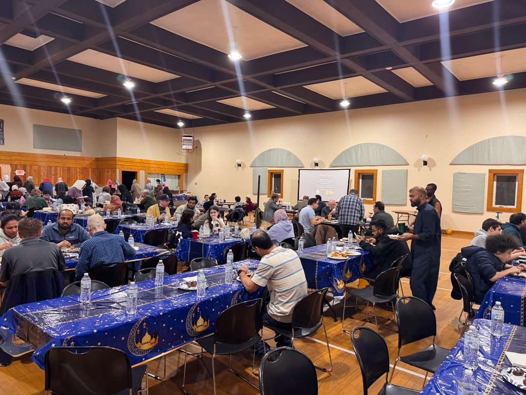 Guests share dinner at long tables with blue tablecloths printed with crescent moons and mosque domes.
