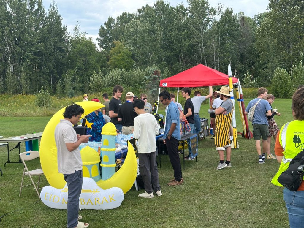 Visitors gather at the MSA table beside a large yellow crescent and dome inflatable reading Eid Mubarak.