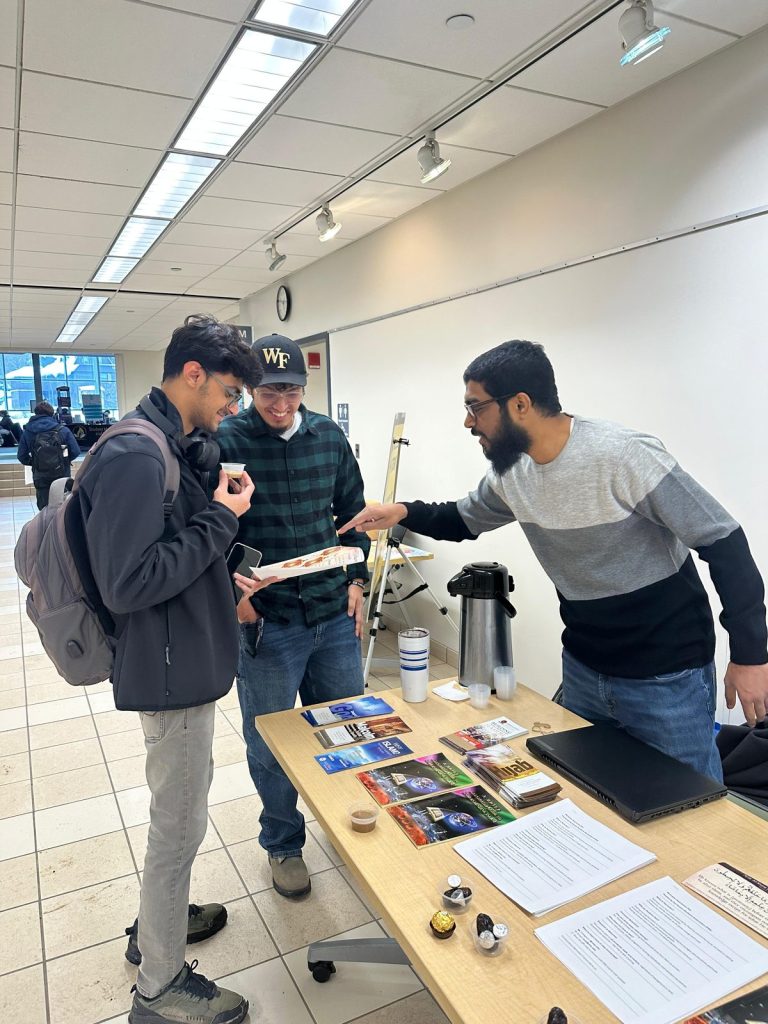 A man at the MSA table points to a visitor's leaflet as another visitor holds a small cup.